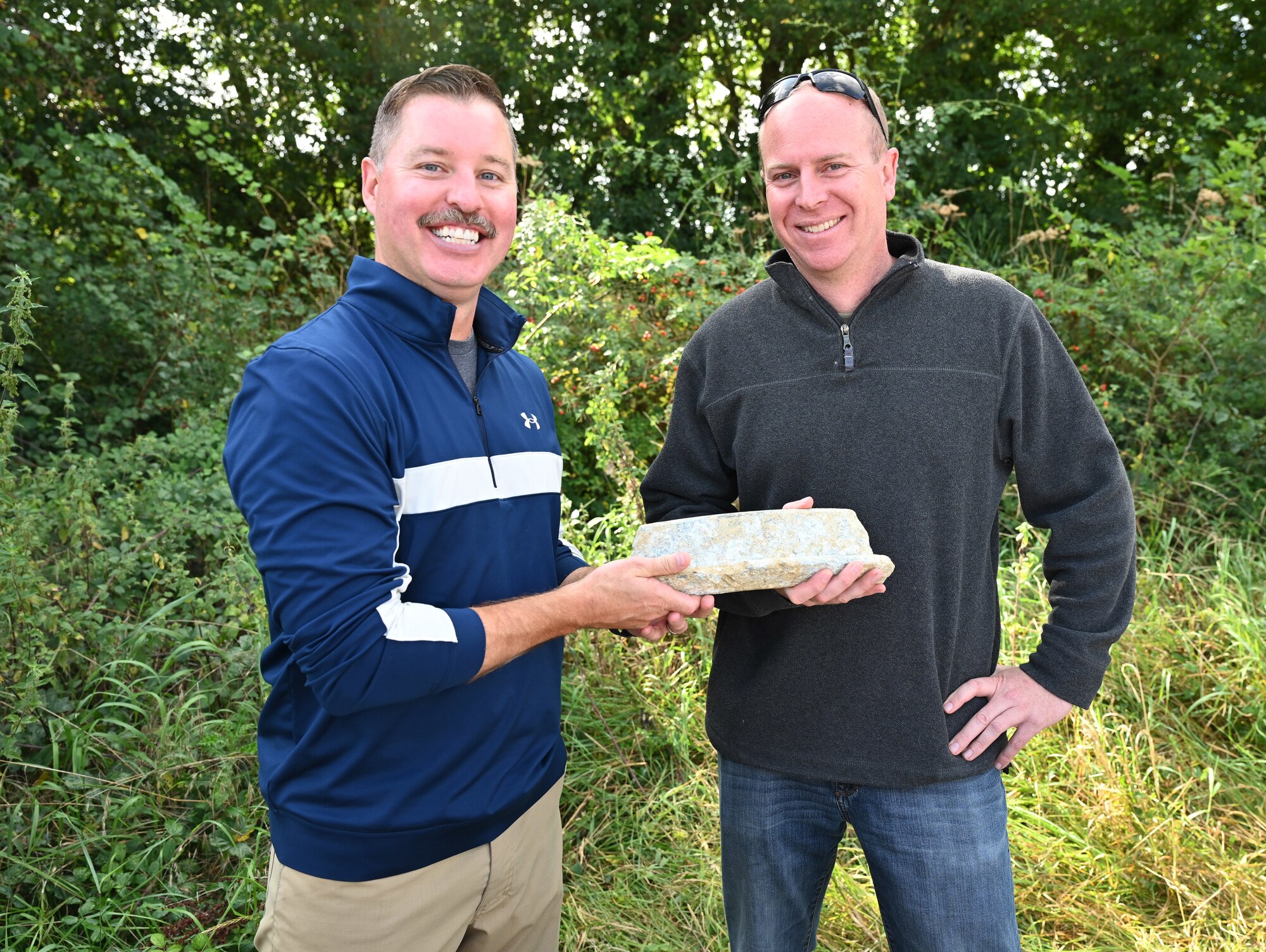 U.S. Air Force Senior Master Sgt. Christopher Staton, left, former 100th Operations Group senior enlisted leader, and Maj. Scott Platow, 351st Air Refueling Squadron director of operations, both Royal Air Force Mildenhall, England, hold a recovered aircraft part from a B-17 Flying Fortress uncovered in a farmer’s field in East Anglia Sept. 19, 2023. The aircraft – “Little Boy Blue” – crashed July 19, 1944, while on its way to bomb a ball-bearing factory and other industrial complexes in Schweinfurt, Germany. An archaeological team from Cotswold Archaeology, partners with the U. S. Defense Prisoner of War/Missing in Action Accounting Agency, led volunteers from a U.K. Ministry of Defence Infrastructure Organization program known as “Operation Nightingale,” on a Missing in Action/Killed in Action recovery operation of the World War II B-17 recovery crash site in September 2023. (U.S. Air Force photo by Karen Abeyasekere)