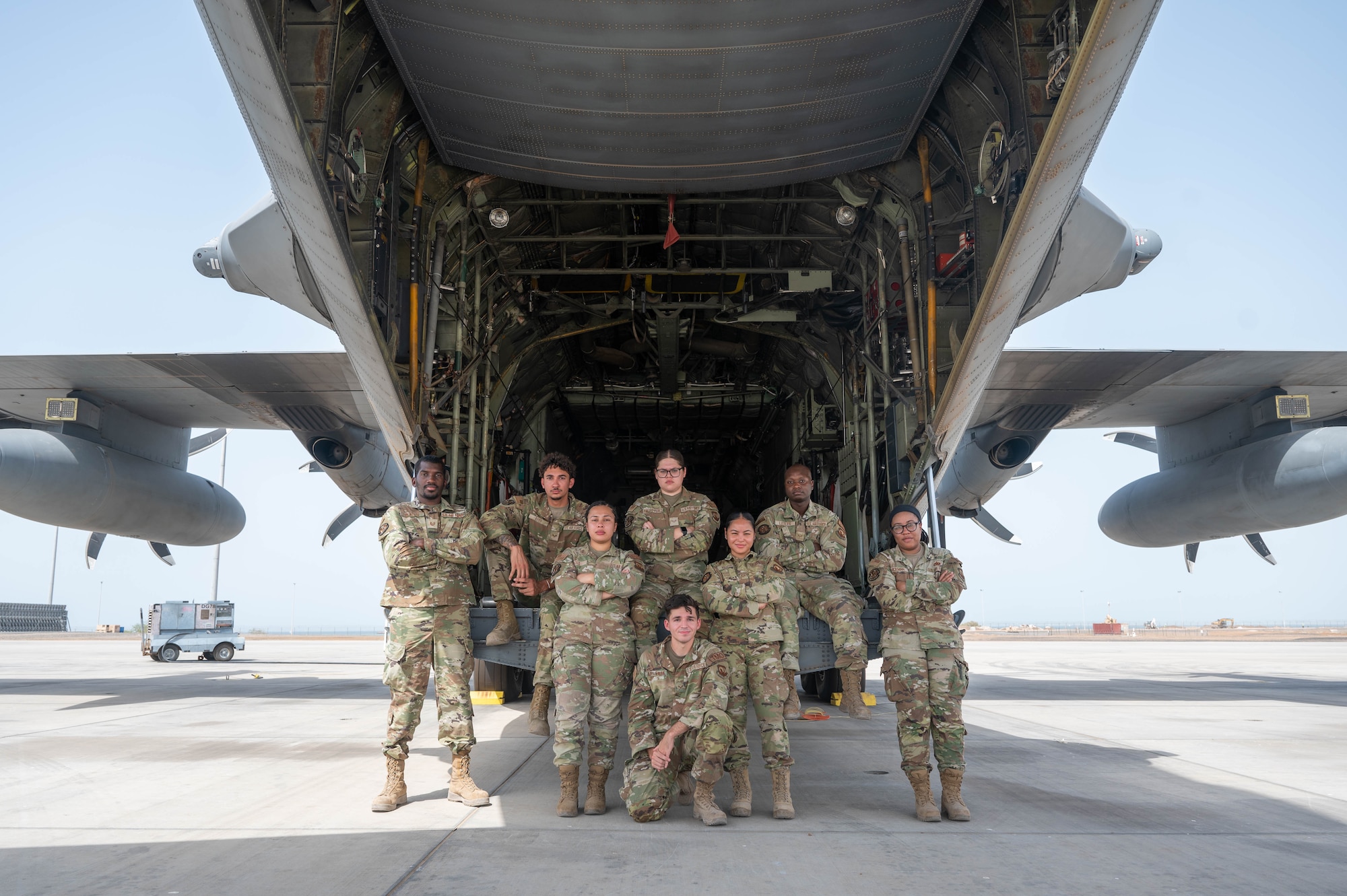 Eight uniformed servicemembers pose for a photo in front of a large aircraft with the rear door lowered.