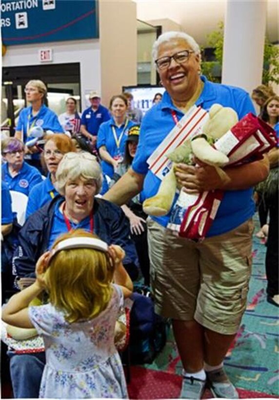 Two women in blue shirts pose together with other ladies in blue shirts in the background mixed in with other people inside an airport.