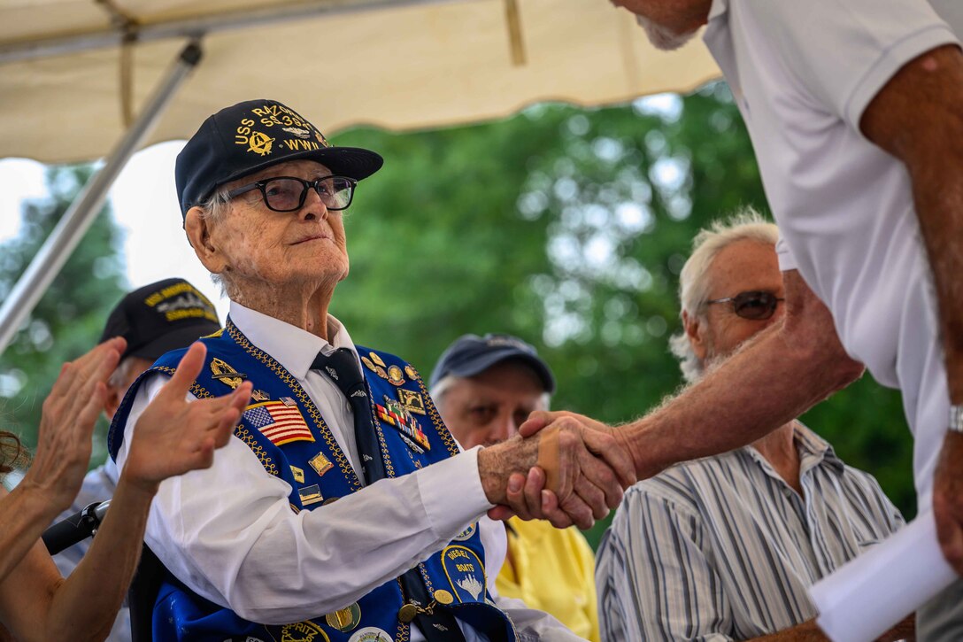 A veteran shakes hands with a civilian during a ceremony under a tent as other people watch.