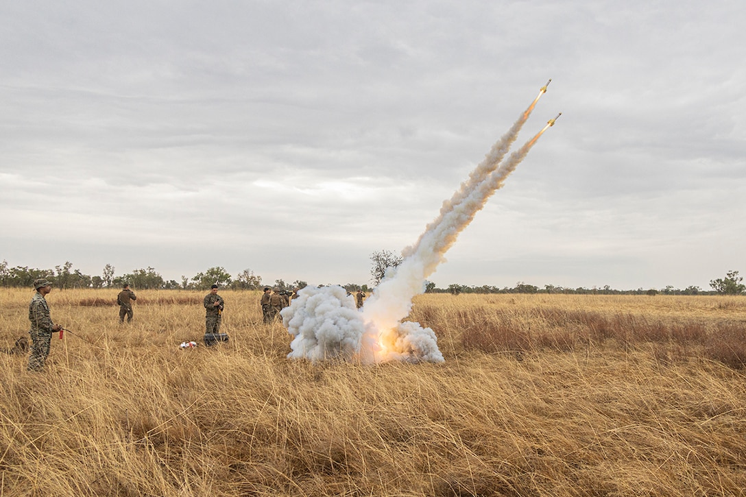 Marines launch missiles from a hay field during training creating smoke.