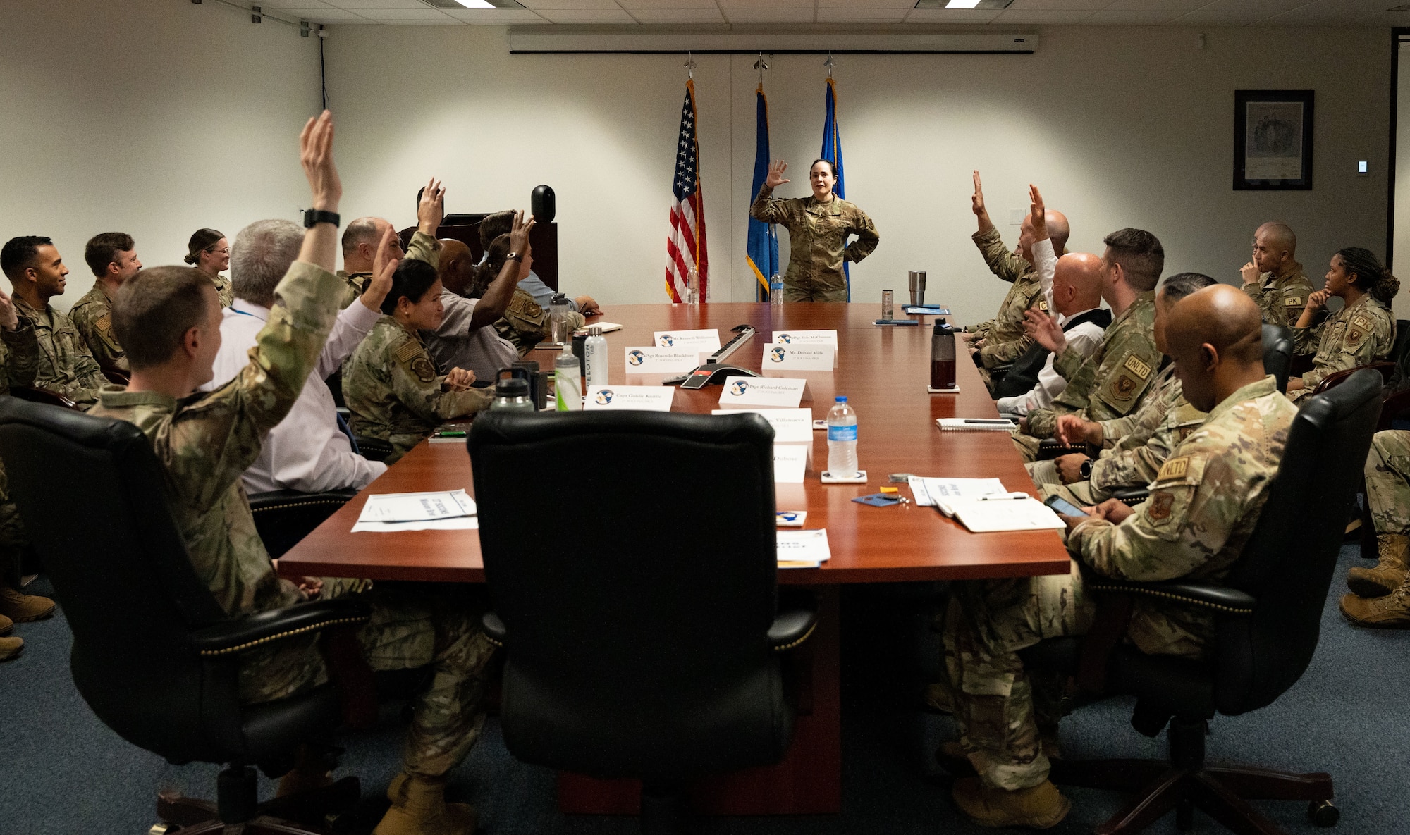 A group of people in business casual and military attire sit around a conference room during a meeting.