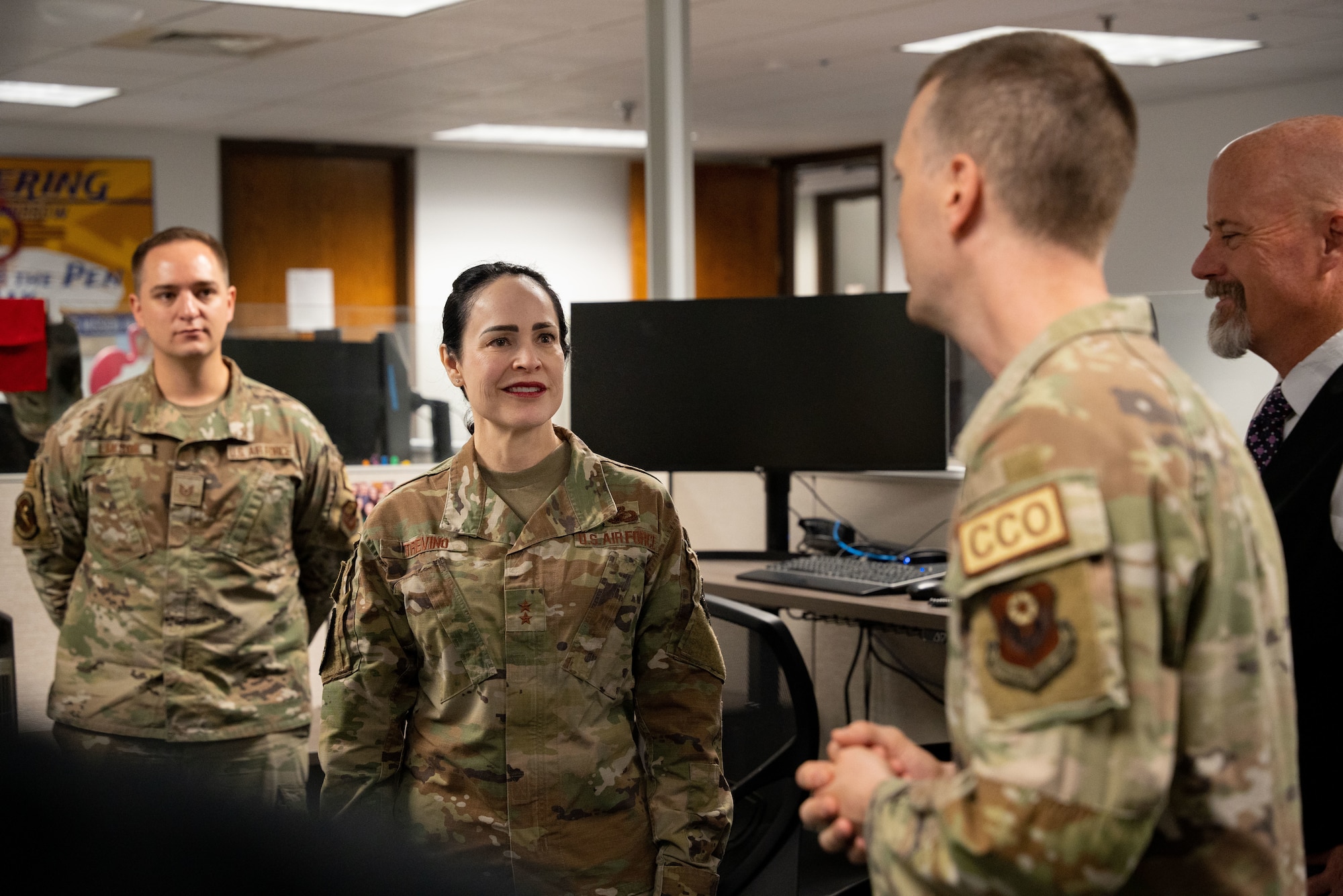 A woman in military uniform speaks to several individuals in military uniform inside an office.