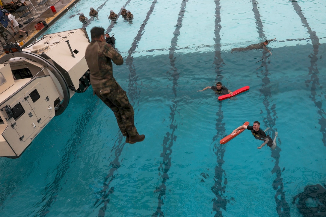 A soldier jumps into a pool next to a floating vehicle as fellow soldiers watch from below.