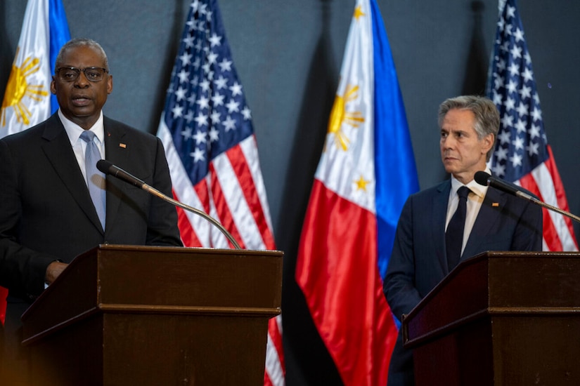 Two people in civilian attire stand at lecterns before a display of U.S. and Philippine flags.