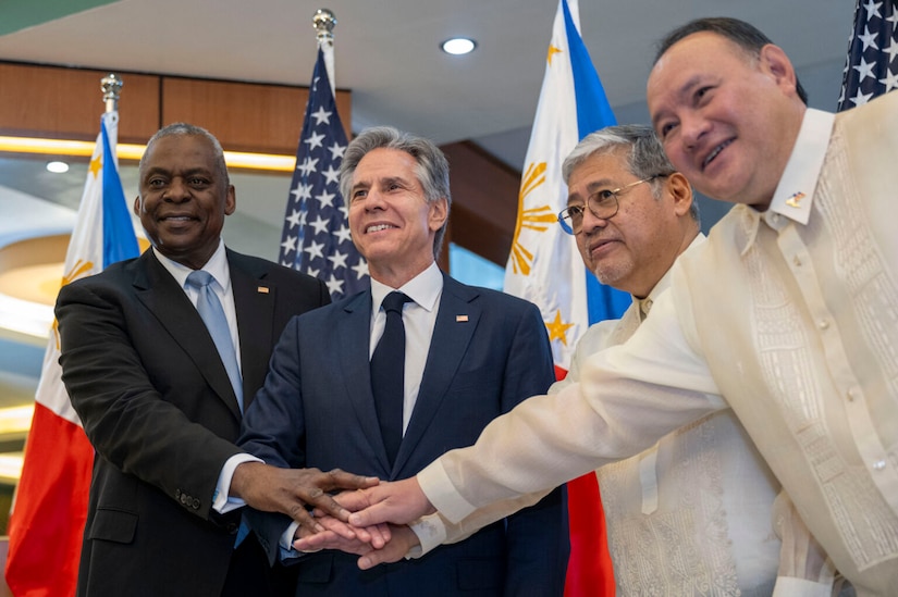 Four people in civilian attire join hands before a display of U.S. and Philippine flags.