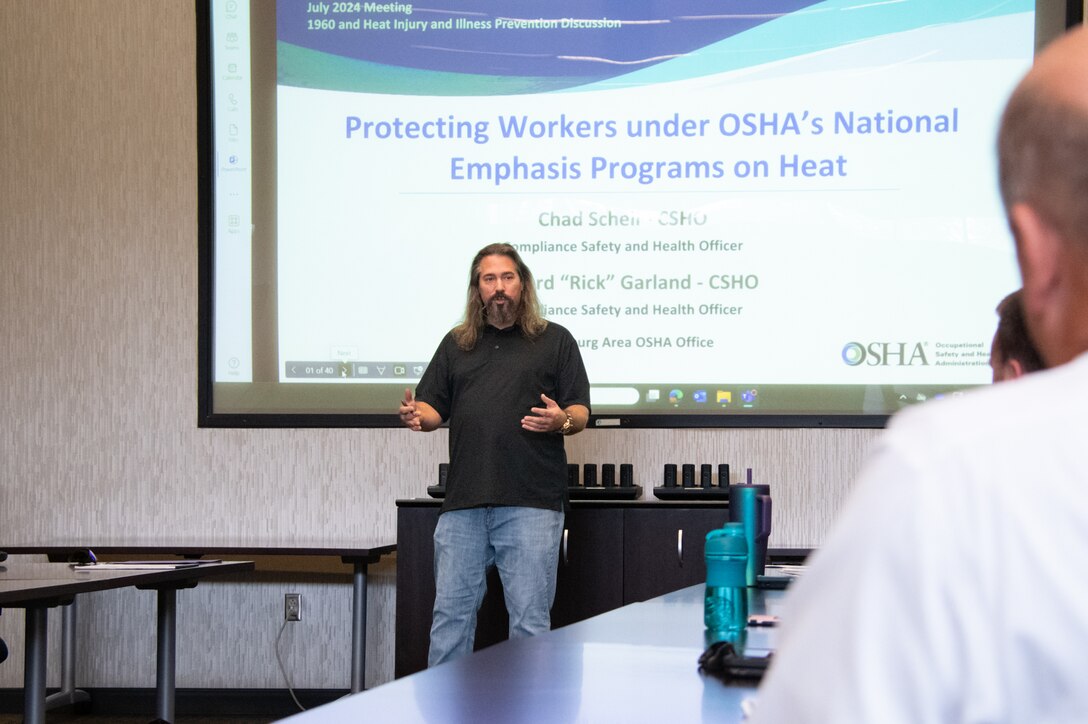 A man stands in front of a projection screen addressing a group of people