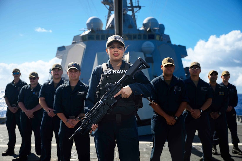 A sailor holds a weapon while posing for a photo with other sailors on a ship.