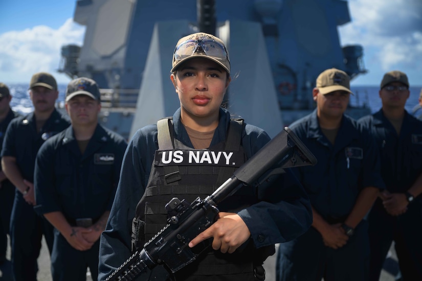 A sailor holds a weapon while posing for a photo with other sailors on a ship.