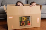Two children crouch inside of a cardboard box.