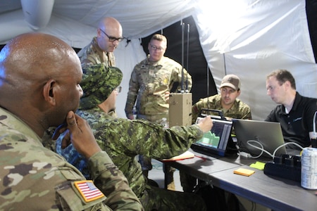 Soldiers gathered around a computer screen inside a field tent