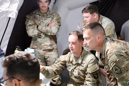 Soldiers gathered around a computer screen inside a field tent