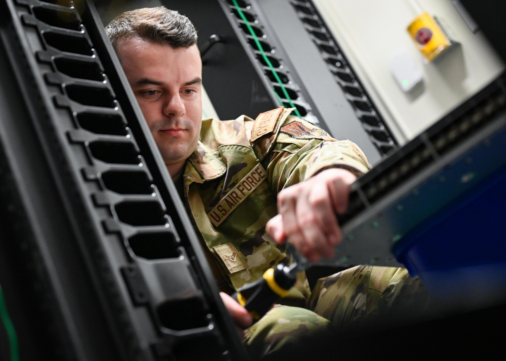 An Airman screw on parts in a server room.