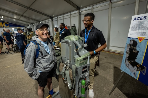 Two men stand and laugh by an ejection seat on display