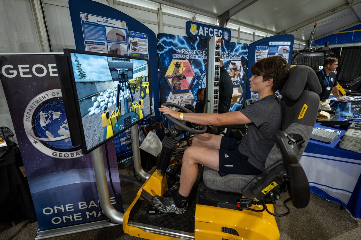 A young airshow attendee sits in a simulation bulldozer with video game monitor moving boulders on screen