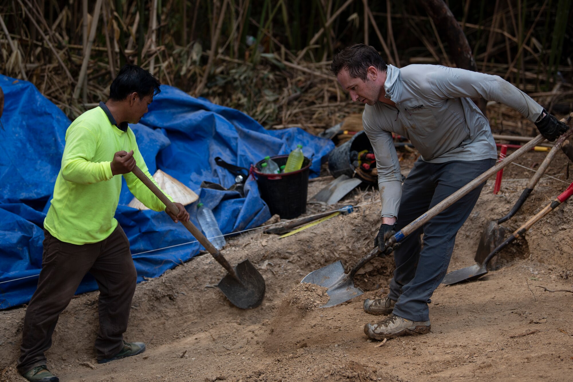 Two men shovel dirt on a hillside.