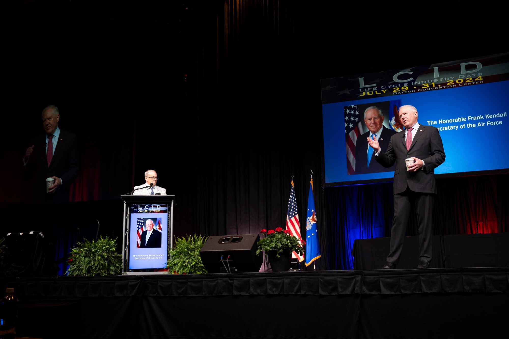 Two men standing on stage, one talking with microphone.
