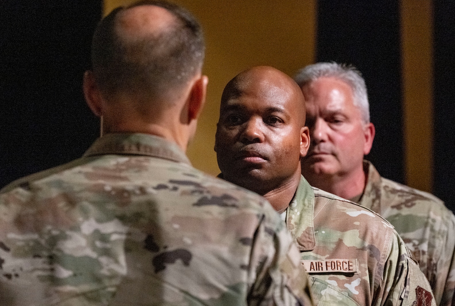 Two Air Force males in uniform stand facing a male Air Force officer in uniform.