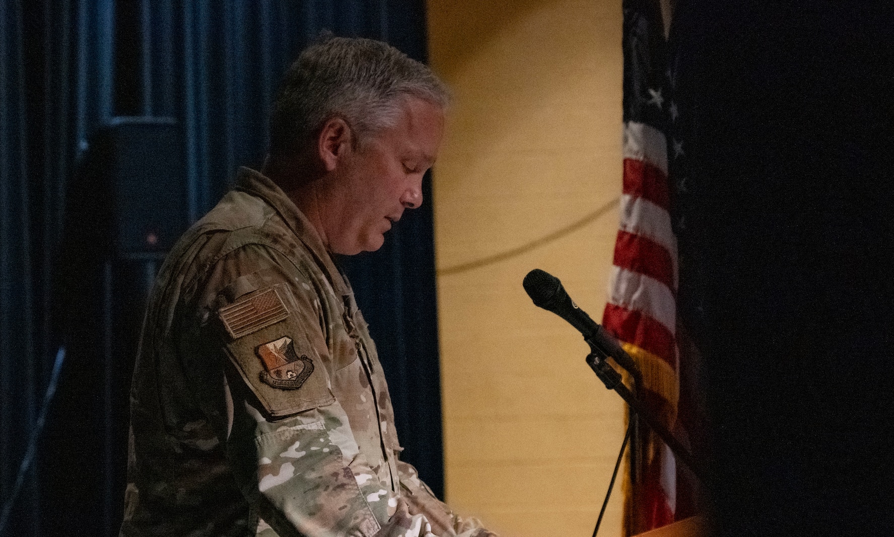 An Air Force male in uniform stands with head bowed at a podium.