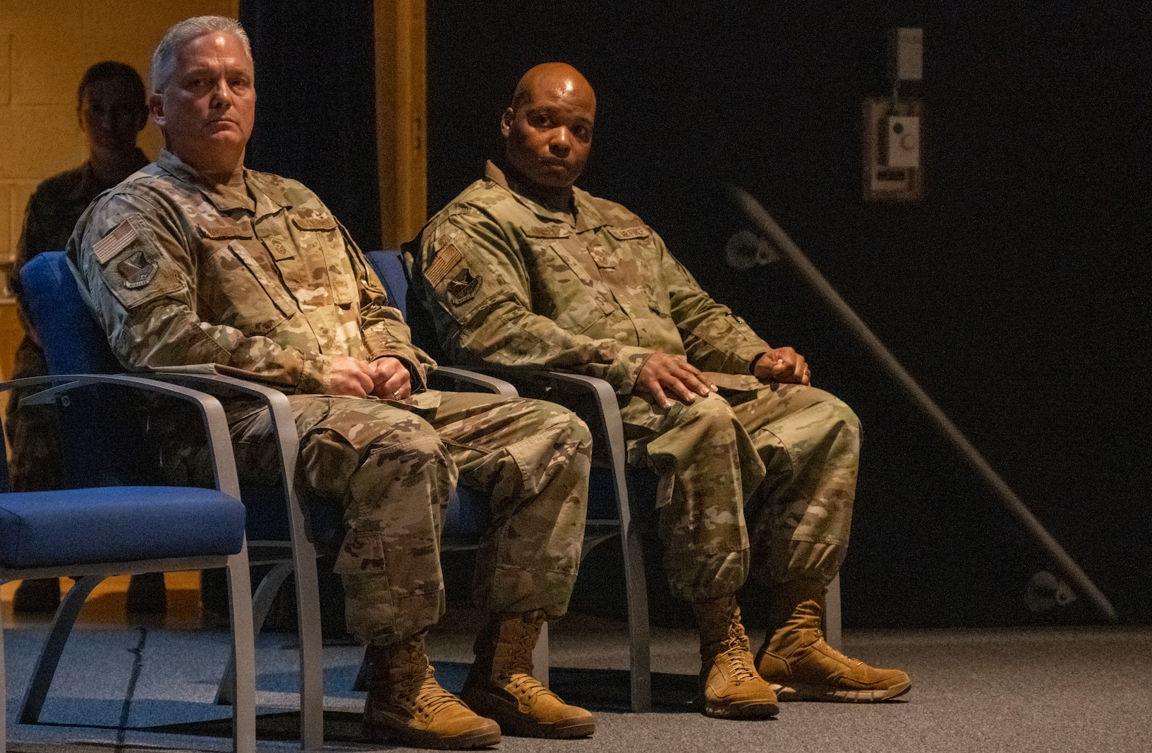 Two male Air Force enlisted in uniform sit side by side.