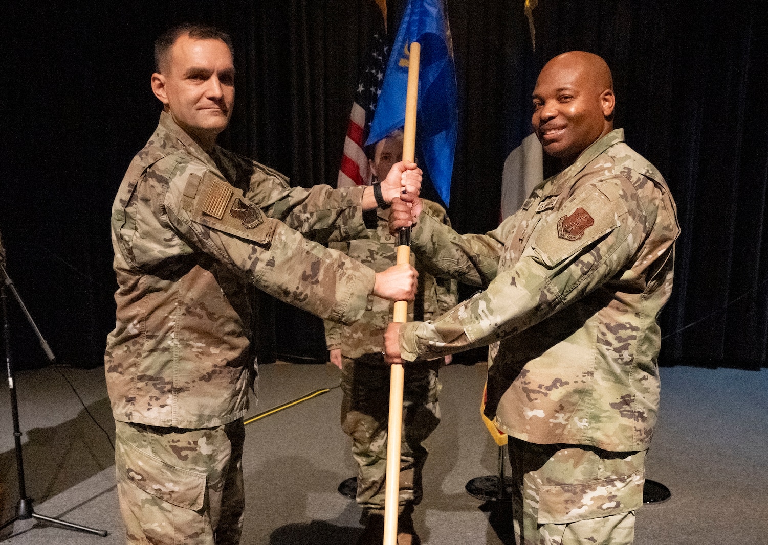 An Air Force officer in uniform holds a guideon along with an enlisted Air Force male while facing forward.