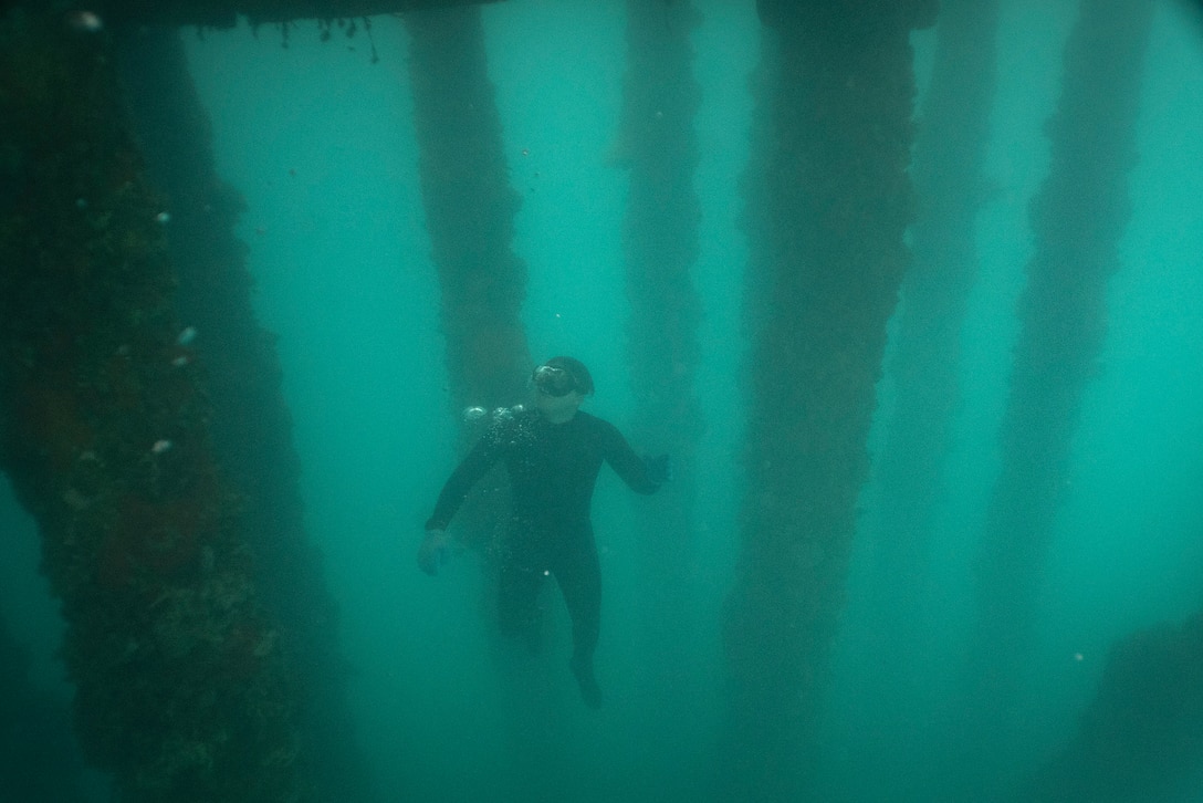 An Army diver swims in murky blue water.