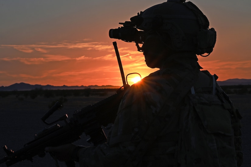 An airman is shown in silhouette at twilight with a low, orange sun in the background.