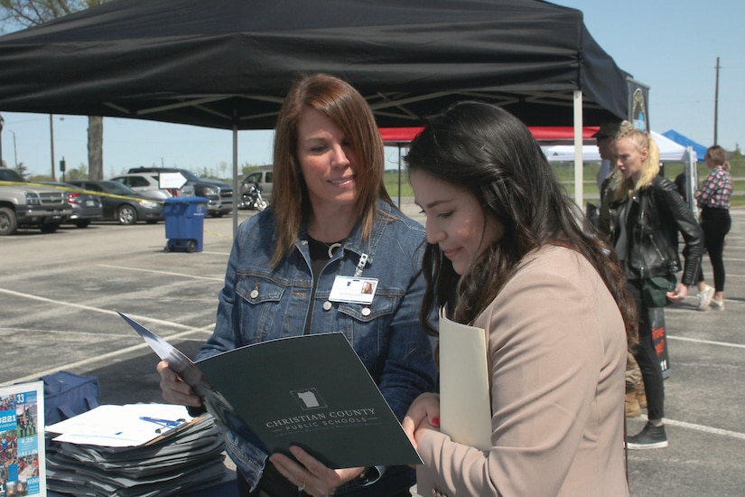 Two women look at paperwork under an outdoor tent.