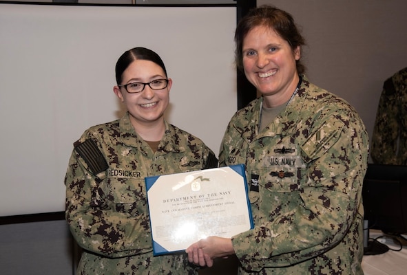 Navy Intelligence Specialist 1st Class Petty Officer Sarah Redsicker, left, a native of Chili, New York and assigned as a Cyber Threat Intelligence (CTI) analyst for Naval Information Warfare Center (NIWC) Atlantic’s Cybersecurity Service Provider (CSSP) team based in Charleston, South Carolina, receives a Navy and Marine Corps Achievement Medal from NIWC Atlantic Commanding Officer Capt. Nicole Nigro April 19 for her work within the CSSP and facilitating cybersecurity exercises, underlining her dedication to protecting critical information systems and enhancing cyber defense capabilities.