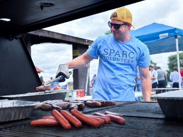 JOINT BASE ANACOSTIA-BOLLING, Washington, D.C. (July 30, 2024) - A volunteer from the Human Resources Group at Strategic Systems Programs (SSP) works the grill at the annual command picnic  Tuesday. This year's event for SSP staff and their families included food, games, a dunk tank, and the car show which featured vehicles--old and new--owned by members of the SSP workforce. The picnic was organized by SSP’s Activity and Recreations Committee (SPARC), an all-volunteer team made up of military and civilians who fundraise and plan MWR events throughout the year. SSP is the Navy command that provides cradle-to-grave lifecycle support for the sea-based leg of the nation’s nuclear triad. (U.S. Navy Photo by Lt. Jennifer Bowman/Released)