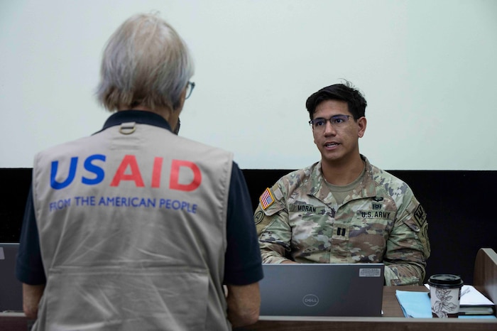 A person wearing a USAID vest talking to a U.S. soldier.