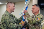 U.S. Navy Capt. Christopher Carmichael, USMEPCOM Western Sector commander, passes the Western Sector colors to Army Command Sgt. Major David Goins, the incoming Western Sector senior enlisted advisor (SEA). during a change of responsibility ceremony, July 31. Goins accepted responsibility as the new SEA of USMEPCOM Western Sector, succeeding Army Command Sgt. Maj. Roger Rendon.