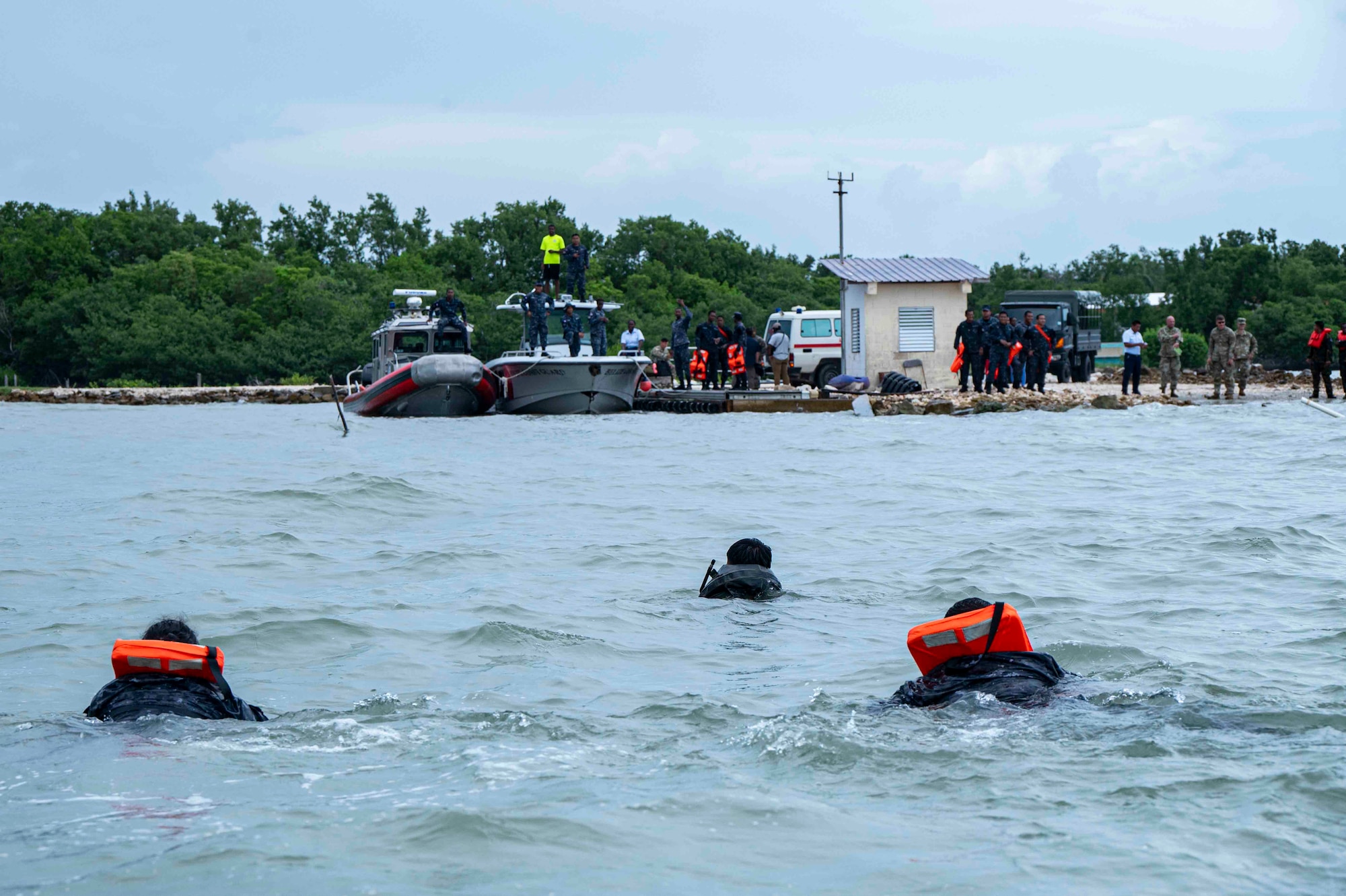 A photo of people swimming to shore where there are boats and bystanders watching.