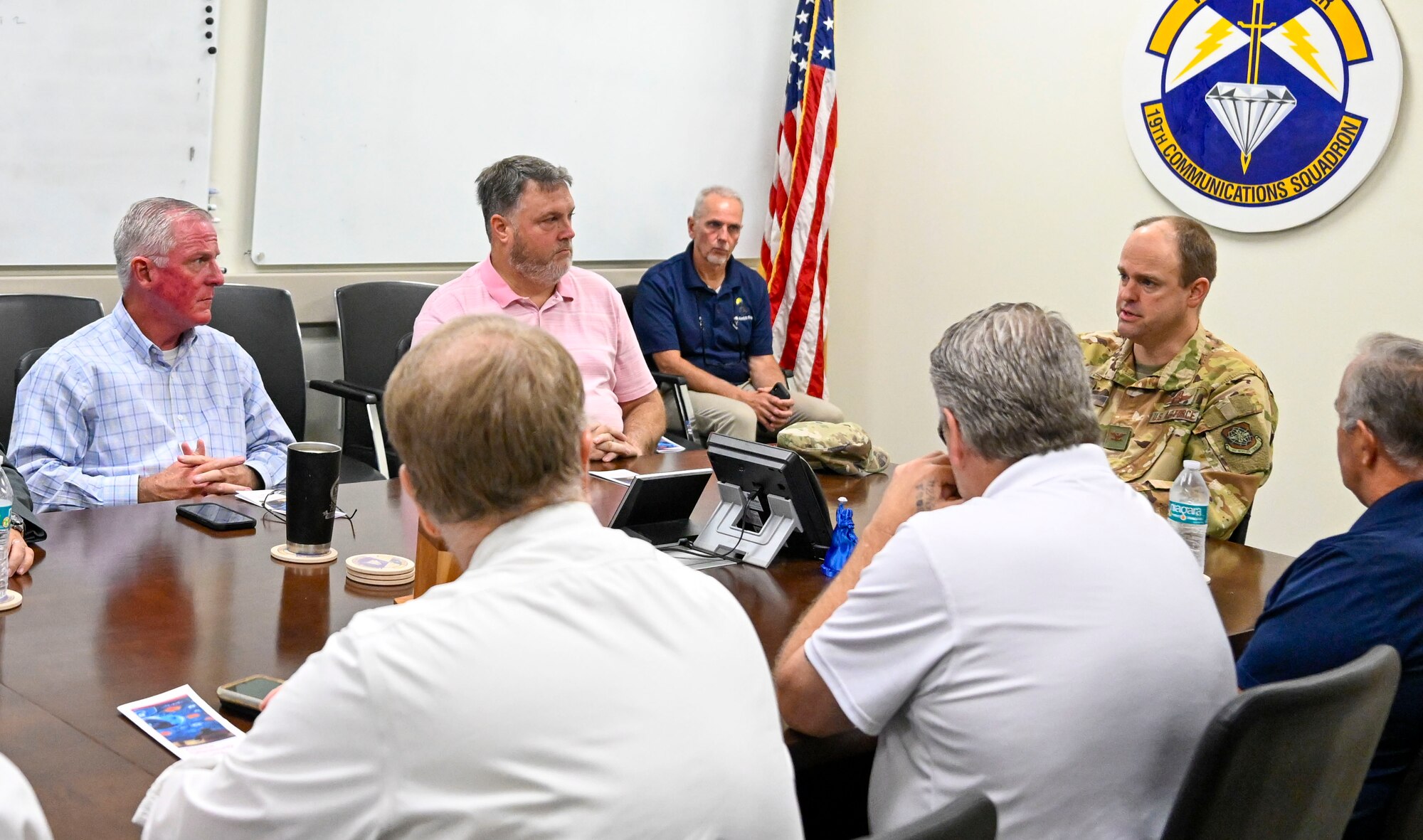 A man in uniform sits and addresses people at a table.