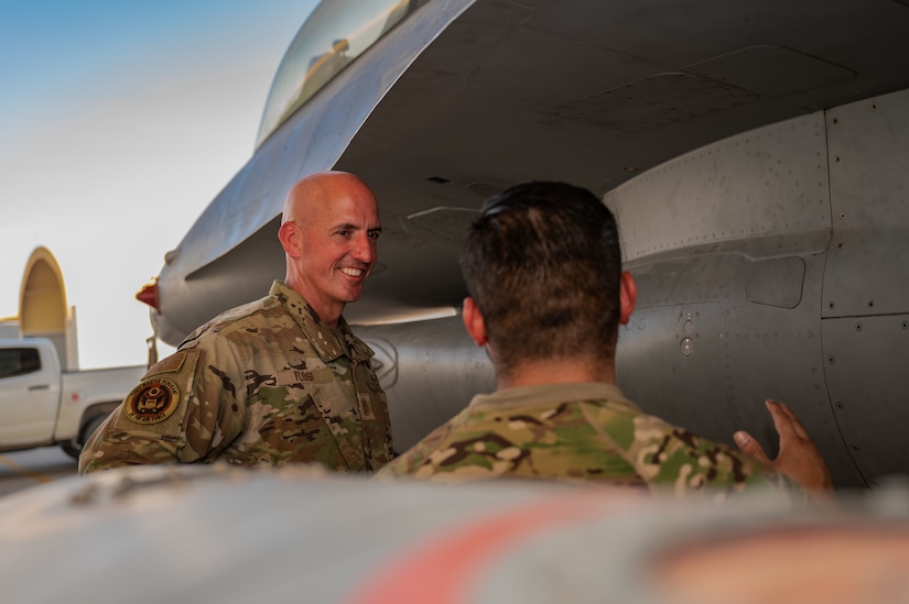 Two airmen talk on a flight line by parked aircraft.