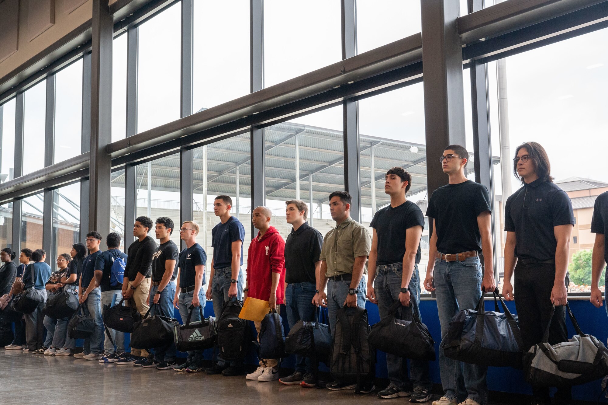 On April 23, 2024, the incoming trainees stand in the Pfingston Reception Center auditorium waiting for more instructions from PRC staff. Every Tuesday, new recruits are bussed in from the San Antonio International Airport to Joint Base San Antonio-Lackland, Texas, to begin seven-and-a-half weeks of Basic Military Training. The PRC represents the start of their transformation from civilians into Airmen. (U.S. Air Force by Ava Leone)
