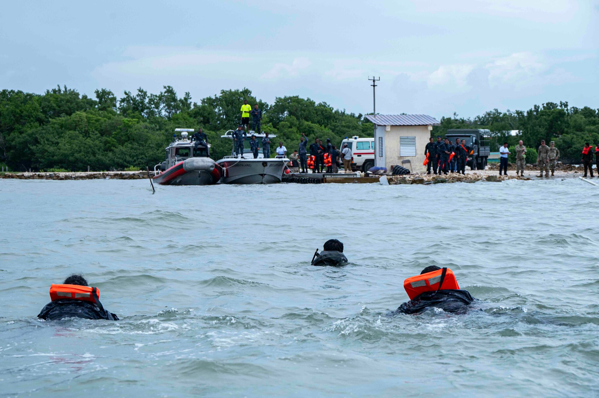 A photo of people swimming to shore where there are boats and bystanders watching.
