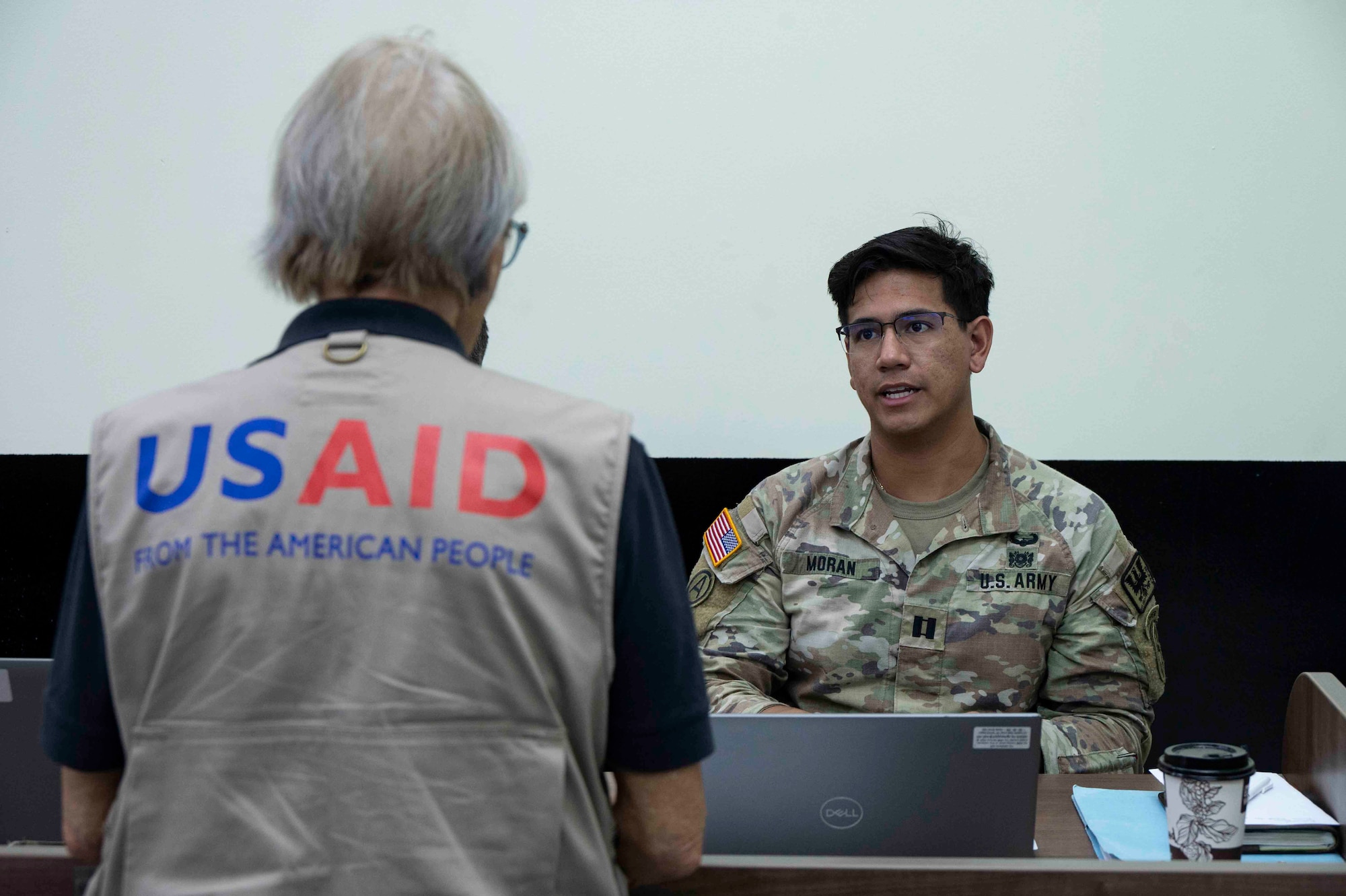 A person wearing a USAID vest talking to a U.S. soldier.