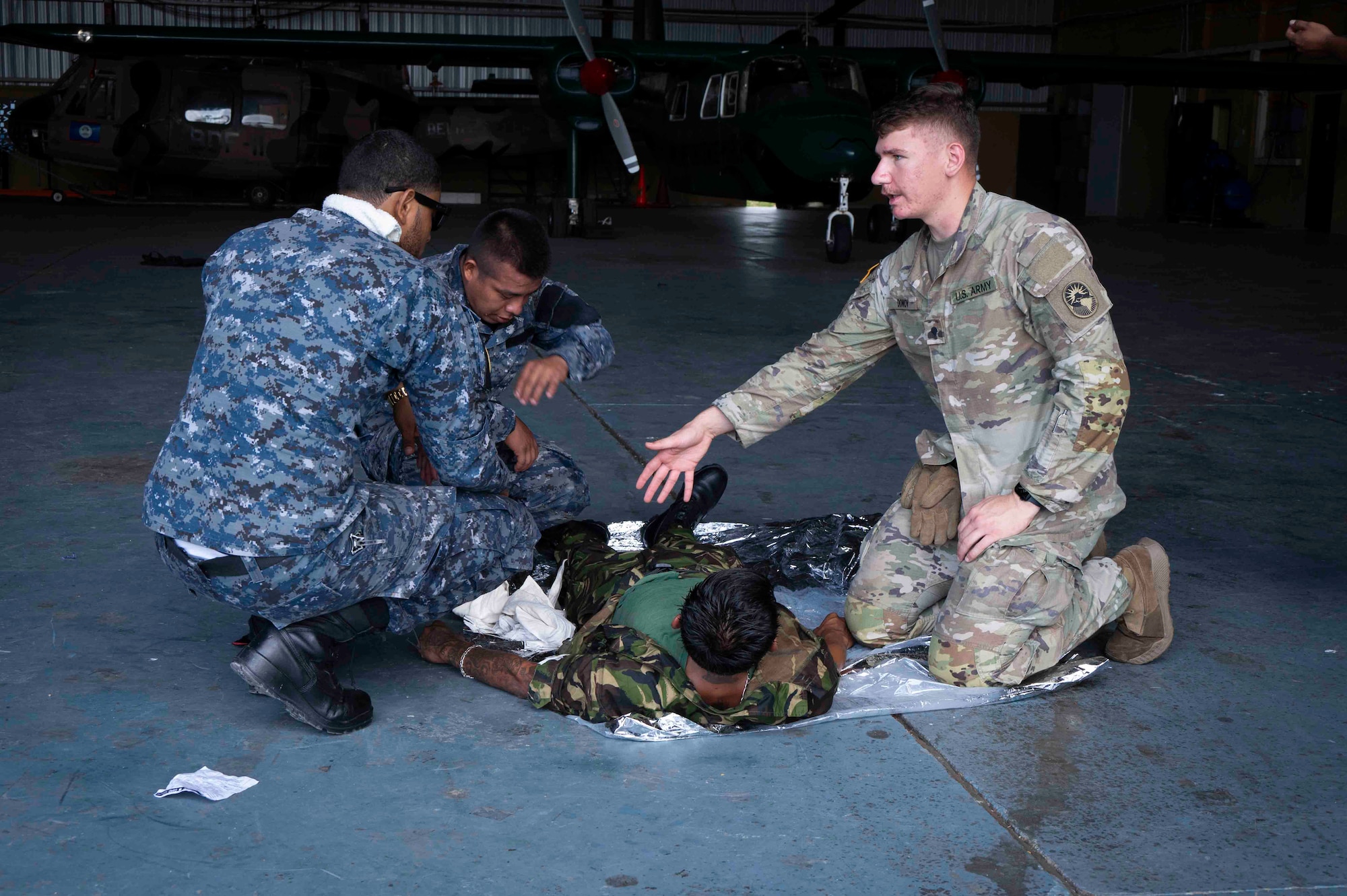 A person pointing a another person's leg explaining tourniquet procedures while two other people watch.