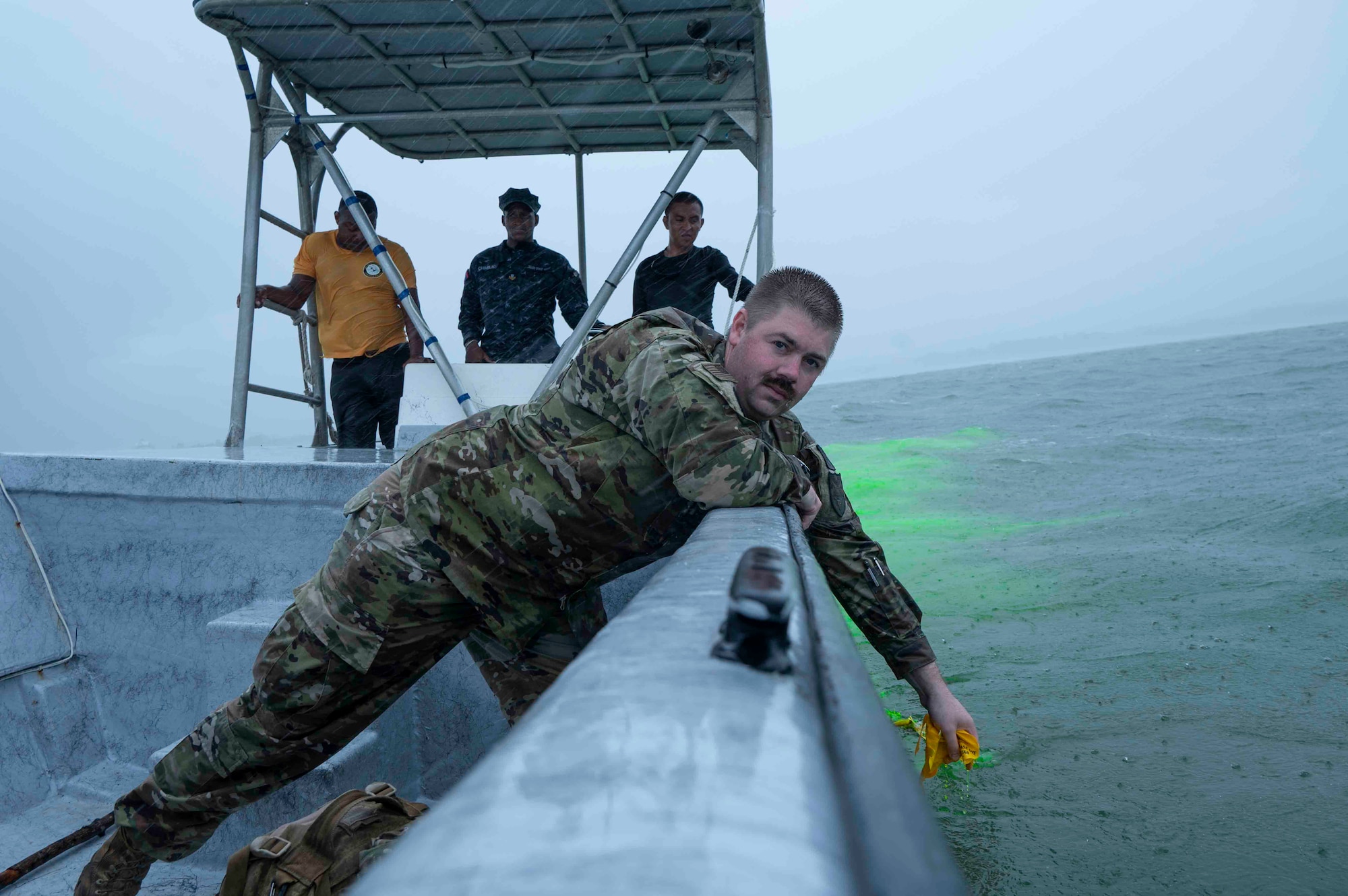 A photo of a person leaning over the edge of a boat and dropping a packet in the water.