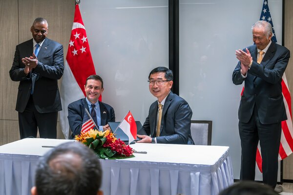Two seated people hold a document as two standing people applaud behind them.