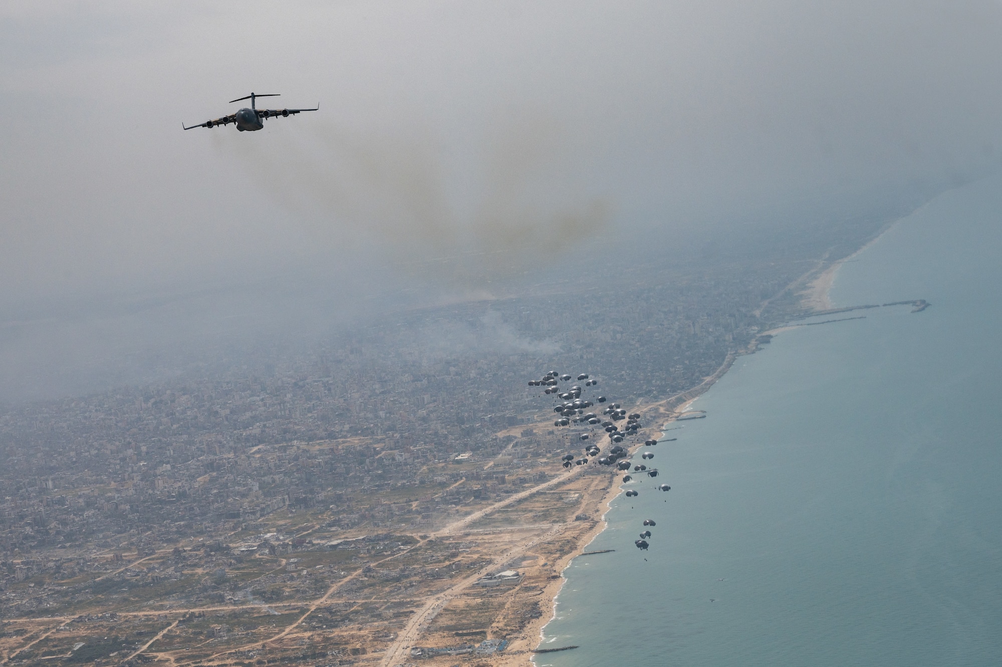 A U.S. Air Force Air Mobility Command C-17 Globemaster III performs an airdrop of humanitarian aid over Gaza, March 29, 2024. Joint Base Charleston C-17s joined coalition aircraft to deliver aid to civilians impacted by the conflict in Gaza. The U.S. Air Force’s rapid global mobility capability enabled the expedited movement of critical, life-saving supplies to Gaza. (U.S. Air Force Photo)