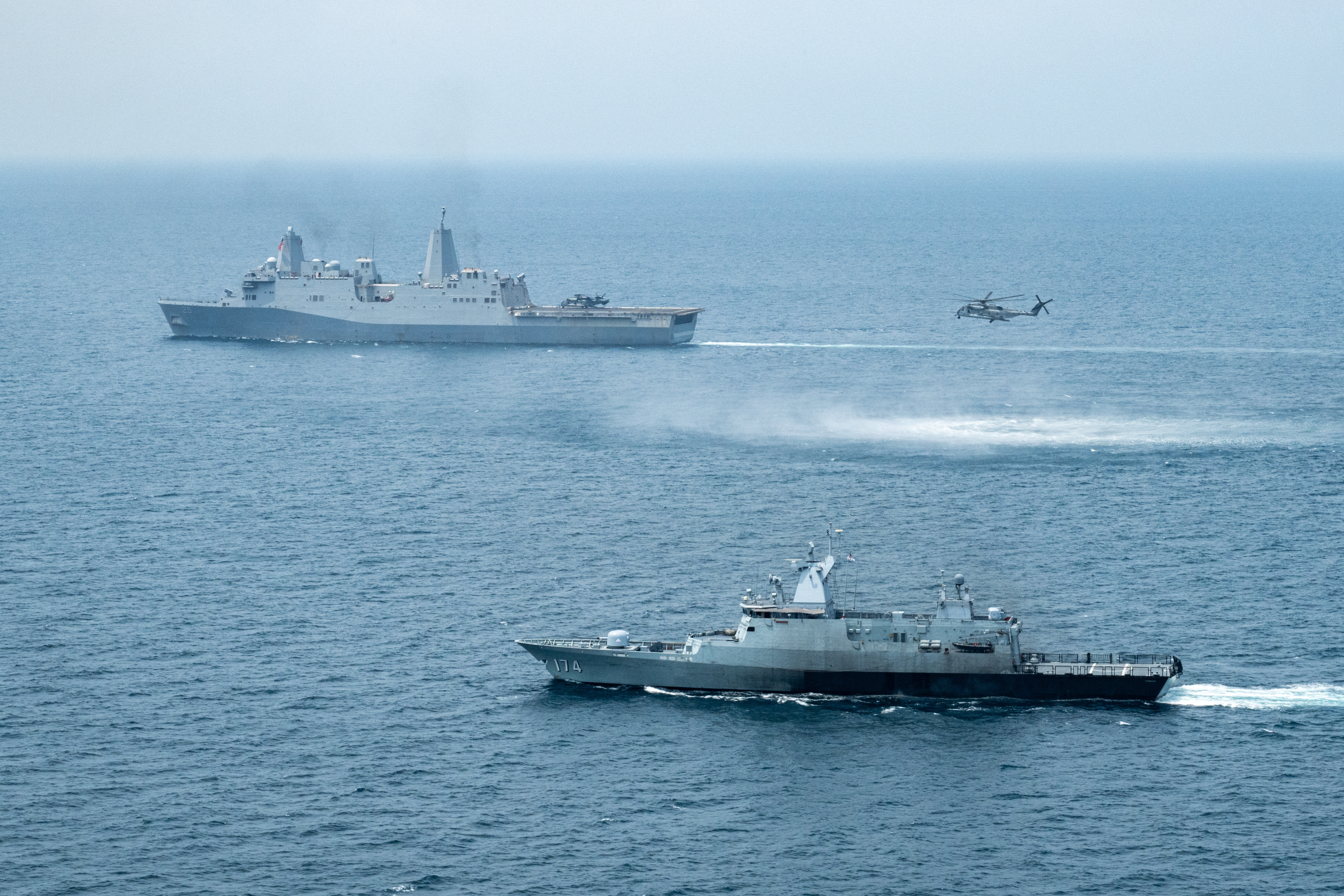 USS Somerset (LPD 25), back, the Malaysian navy patrol vessel KD Terengganu (F174), front, and a USMC helicopter from VMM-165 are underway during Tiger Strike 24 in the South China Sea.