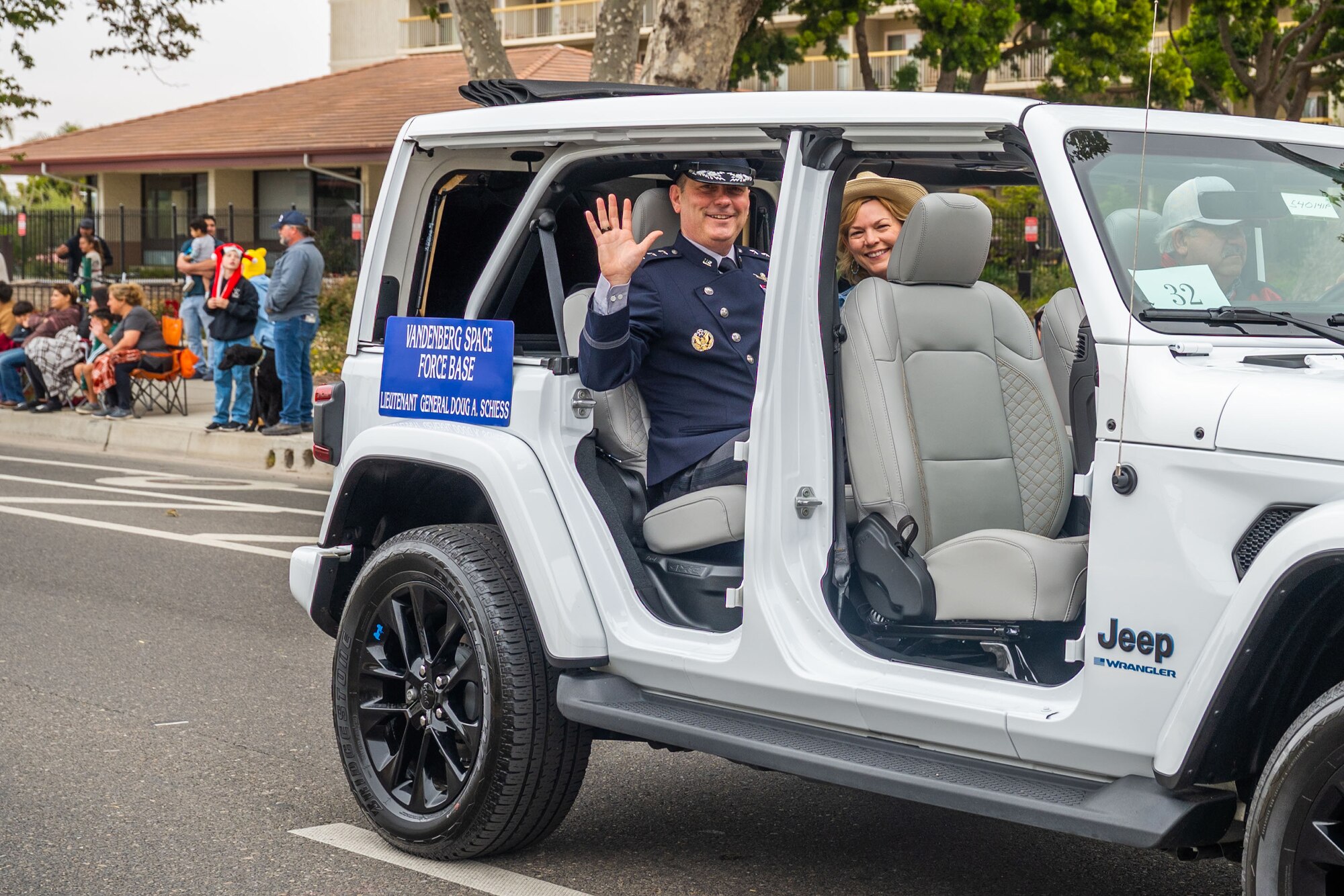 A military married couple waves to viewers of a parade from the back of a vehicle.