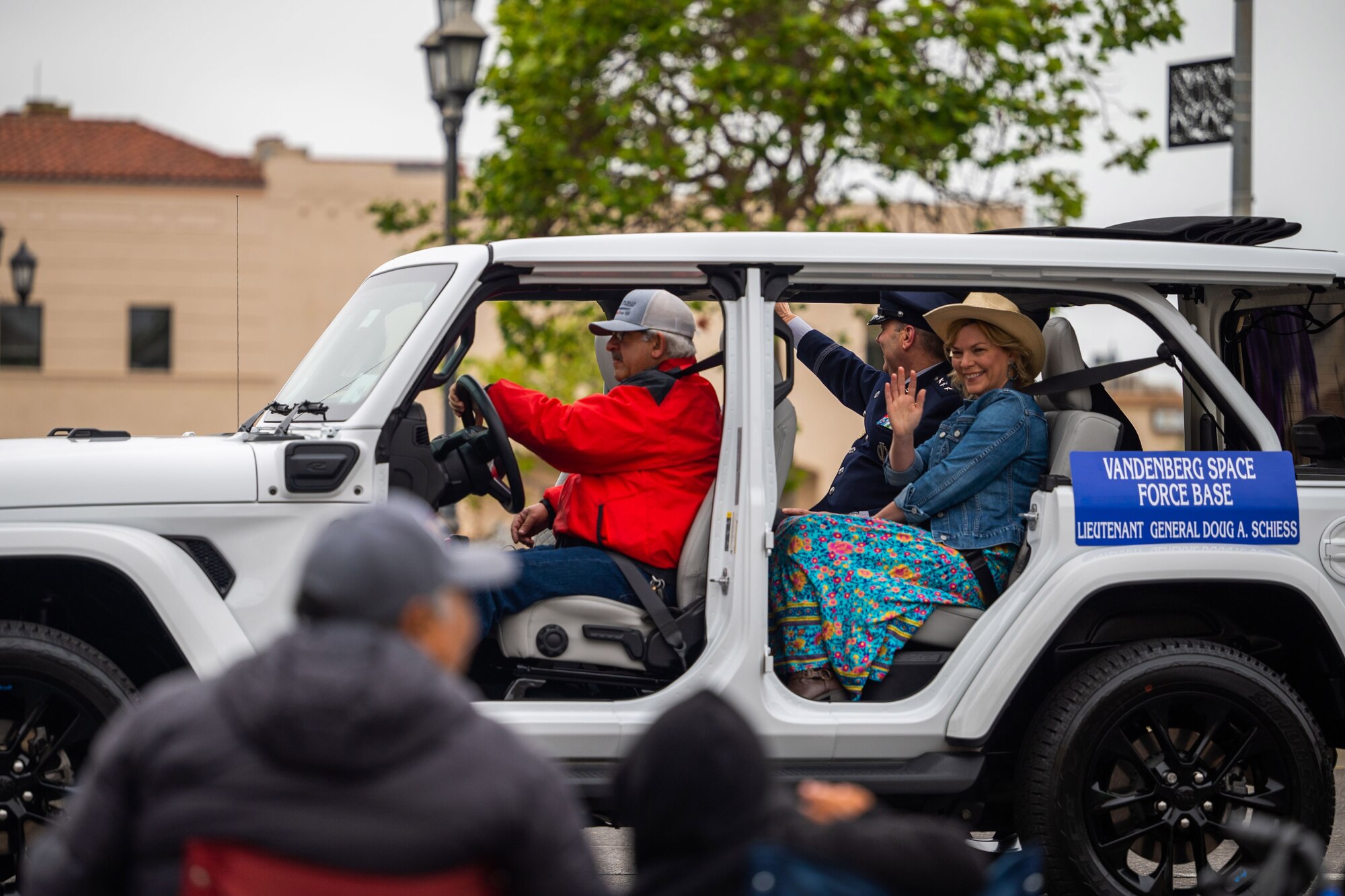 A military married couple waves to crowd members from the back of a vehicle during a parade.