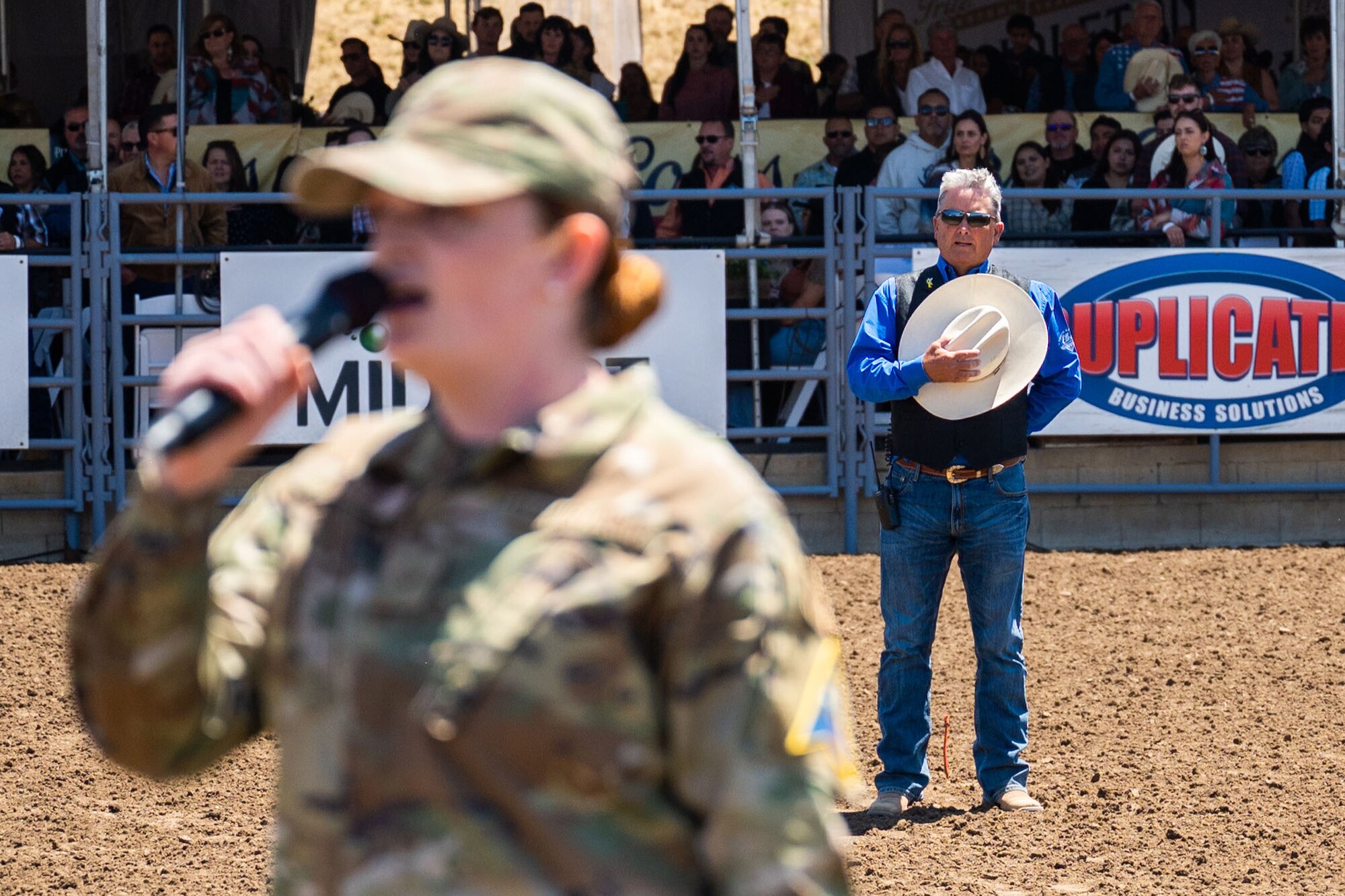 a man puts his hat over his heart as a U.S. Air Force Airman sings the national anthem in front of him.