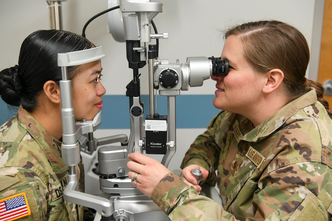 An airman looks through a device to examine a soldier’s eyes.