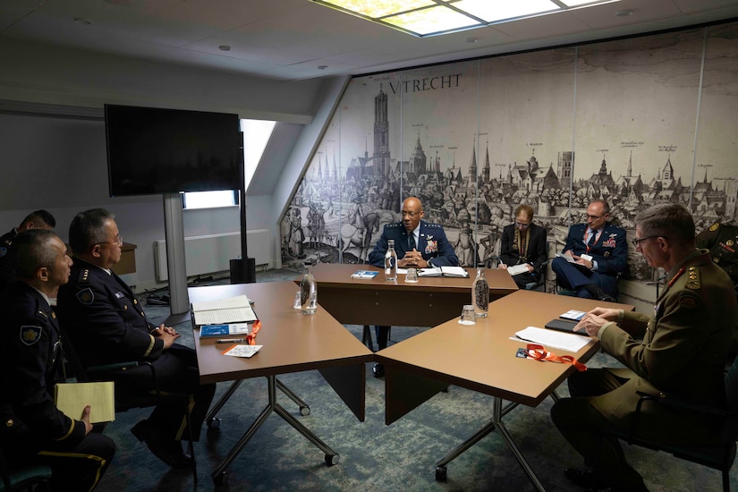 An Air Force officer in uniform sits at a table next to foreign military officers.