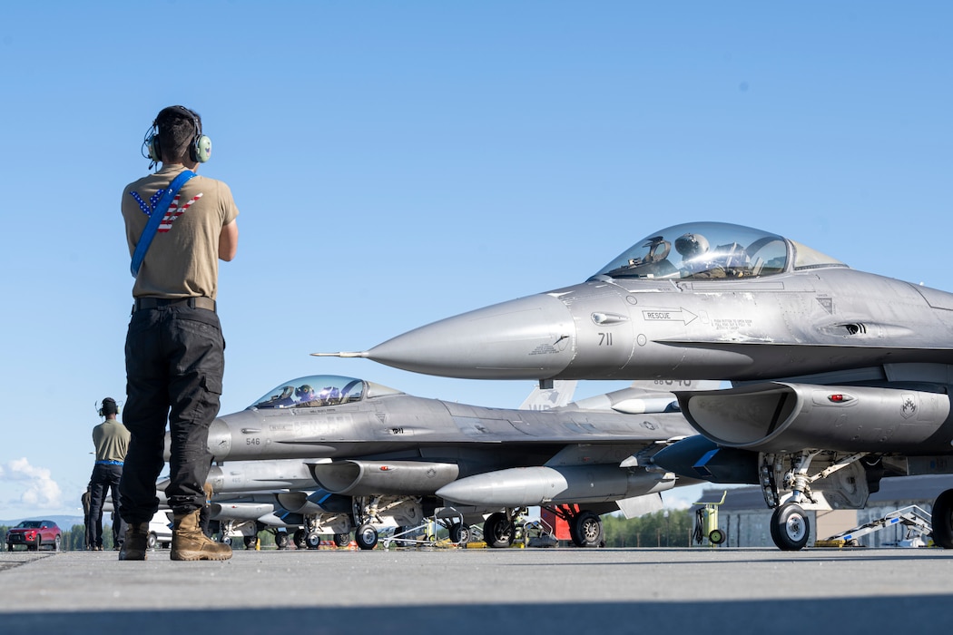 F-16 aircraft and maintainers are lined up preparing for takeoff.