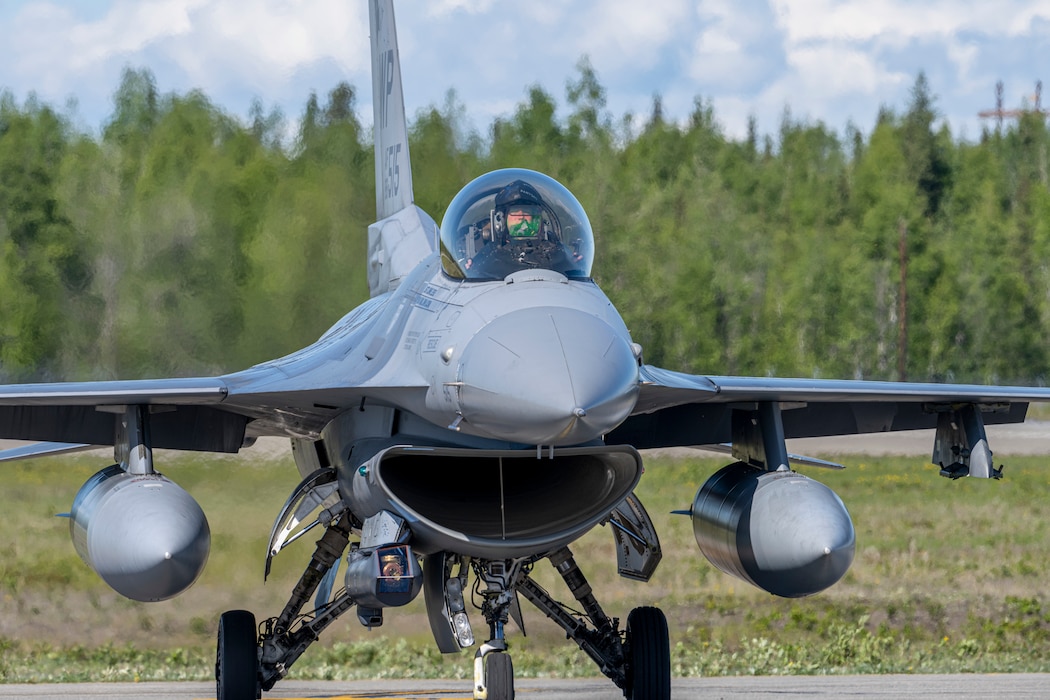 An F-16 aircraft taxies on the flighline. The nose of the aircraft is facing the photographer.